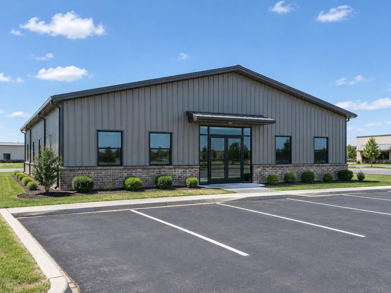Illustrative building concept — AI-generated, not a completed Outlaw Building Co. project AI-generated illustration: Gray commercial metal building with a glazed entrance, brick wainscot and marked parking area. Not a completed Outlaw Building Co. project.